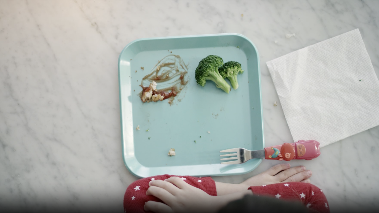 A minimal food photo with an empty plate and utensils beside scraps of vegetables.